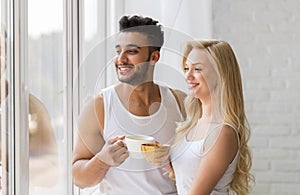 Young Beautiful Couple Stand Near Big Window, Drink Morning Coffee Cup, Happy Smile Hispanic Man Woman