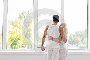 Young Beautiful Couple Stand Near Big Window Embrace, Happy Smile Hispanic Man And Woman Lovers Hug
