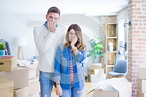 Young beautiful couple standing at new home around cardboard boxes looking stressed and nervous with hands on mouth biting nails
