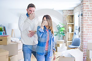 Young beautiful couple standing at new home around cardboard boxes smelling something stinky and disgusting, intolerable smell,