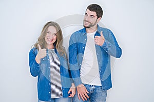 Young beautiful couple standing together over white isolated background doing happy thumbs up gesture with hand