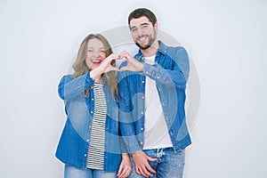 Young beautiful couple standing together over white isolated background smiling in love doing heart symbol shape with hands
