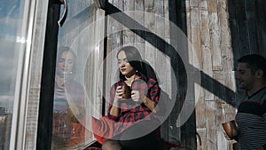 A young beautiful couple standing in a winter frosty day near a large window and drinking hot morning coffee. Happy