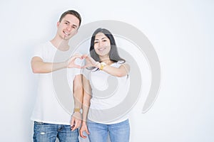 Young beautiful couple wearing casual t-shirt standing over isolated white background smiling in love showing heart symbol and