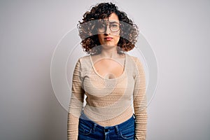 Young beautiful curly arab woman wearing casual t-shirt and glasses over white background skeptic and nervous, frowning upset