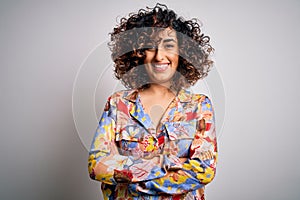 Young beautiful curly arab woman wearing floral colorful shirt standing over white background happy face smiling with crossed arms
