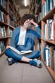 Young beautiful curly girl in glasses and blue suit sitting with books in the library.