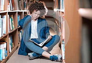 Young beautiful curly girl in glasses and blue suit sitting with books in the library.