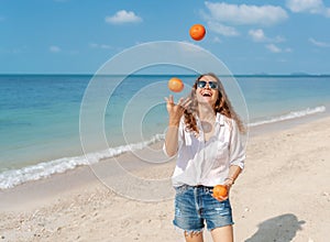 Young beautiful curly woman girl juggles oranges and has fun on a swing on a tropical beach. Vacation and travel concept