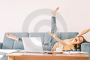 Young beautiful curly woman happy lies on the sofa, on the table a laptop and working papers, success in work