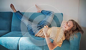 Young beautiful curly woman happy lying on the sofa and looking at the camera with a happy smile