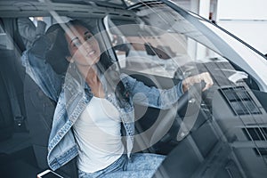 Young and beautiful. Cute girl with black hair trying her brand new expensive car in the automobile salon