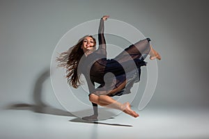 Young beautiful dancer in black dress posing on a dark gray studio background