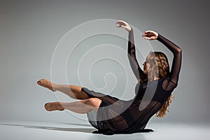 Young beautiful dancer in black dress posing on a dark gray studio background