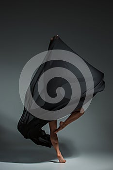 Young beautiful dancer in black dress posing on a dark gray studio background