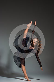 Young beautiful dancer in black dress posing on a dark gray studio background