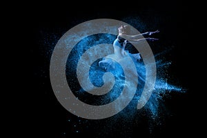 Young beautiful dancer jumping into blue powder cloud