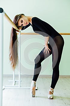 Young beautiful dancer posing in studio wit Ballet bar on tiptoe. Modern brunette.
