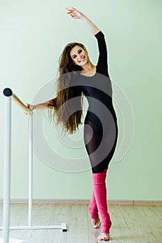 Young beautiful dancer posing in studio wit Ballet bar on tiptoe. Modern brunette.