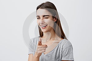 Young beautiful dark-haired caucasian girl with long hair in stylish plain t-shirt smiling with teeth, winking