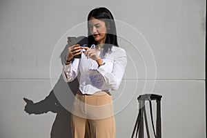 Young, beautiful, dark-haired woman is consulting her mobile phone at the entrance door of the building where she works as an