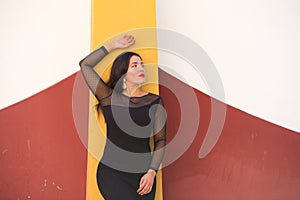 Young, beautiful, dark-haired woman is dressed elegantly in a black dress with transparencies. The girl leans against the wall