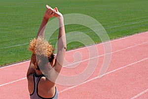 Sports exercises and stretching or preparing a runner to start at the stadium. A young beautiful dark-skinned girl in a gray tank