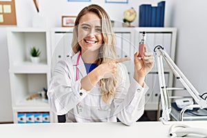 Young beautiful doctor woman holding electronic cigarette at the clinic smiling happy pointing with hand and finger