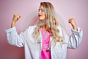 Young beautiful doctor woman using stethoscope over pink  background showing arms muscles smiling proud