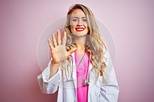 Young beautiful doctor woman using stethoscope over pink  background showing and pointing up with fingers number five