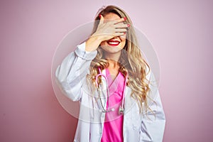 Young beautiful doctor woman using stethoscope over pink  background smiling and laughing with hand on face covering eyes