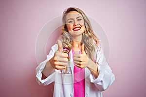 Young beautiful doctor woman using stethoscope over pink isolated background approving doing positive gesture with hand, thumbs up