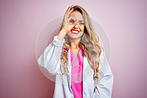 Young beautiful doctor woman using stethoscope over pink isolated background doing ok gesture with hand smiling, eye looking