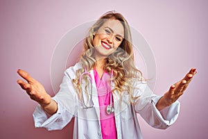 Young beautiful doctor woman using stethoscope over pink isolated background looking at the camera smiling with open arms for hug