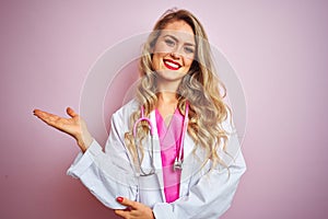Young beautiful doctor woman using stethoscope over pink isolated background smiling cheerful presenting and pointing with palm of