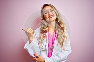 Young beautiful doctor woman using stethoscope over pink isolated background smiling with happy face looking and pointing to the