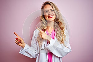 Young beautiful doctor woman using stethoscope over pink isolated background smiling and looking at the camera pointing with two