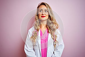 Young beautiful doctor woman using stethoscope over pink isolated background smiling looking to the side and staring away thinking