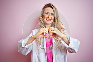 Young beautiful doctor woman using stethoscope over pink isolated background smiling in love doing heart symbol shape with hands