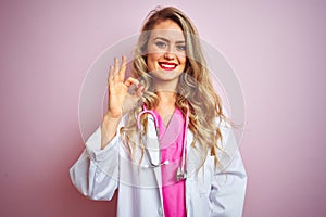 Young beautiful doctor woman using stethoscope over pink isolated background smiling positive doing ok sign with hand and fingers