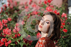 Young beautiful dreamy woman with closed eyes posing in the rose garden. Outdoor fashion portrait of romantic girl with hard light