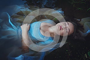 Young beautiful drowned woman in blue dress lying in the river