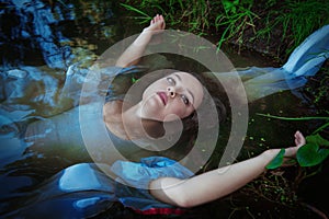 Young beautiful drowned woman in blue dress lying in the water photo