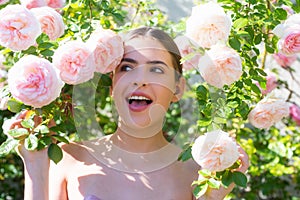 Young beautiful elegant fashion lady white summer dress posing in pink spring blossom roses garden. Close up portrait.