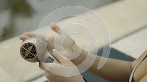 Young and beautiful European girl in a swimsuit using an electric device for arms skin care