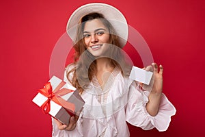 Young beautiful european stylish brunette woman wearing white blouse and fashionable hat isolated over red background