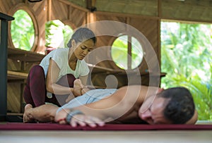 Young beautiful and exotic Asian Indonesian therapist woman giving traditional Thai massage to man relaxed at tropical wellness