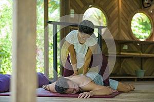 Young beautiful and exotic Asian Indonesian therapist woman giving traditional Thai massage to man relaxed at tropical wellness