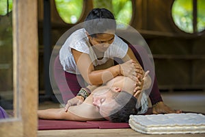 Young beautiful and exotic Asian Indonesian therapist woman giving traditional Thai massage to man relaxed at tropical wellness