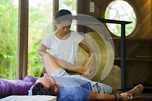 Young beautiful and exotic Asian Indonesian therapist woman giving traditional Thai massage to man relaxed at tropical wellness